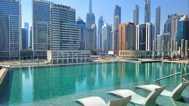 Ein Poolbereich mit Liegestühlen, freier Sicht auf den Stadtpanoramablick und modernen Hochhäusern.