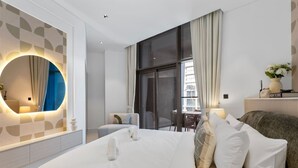 Ein modernes Hotelzimmer mit einem großen Bett, einem runden Spiegel, einem Schreibtisch und Blick auf die Stadt.
