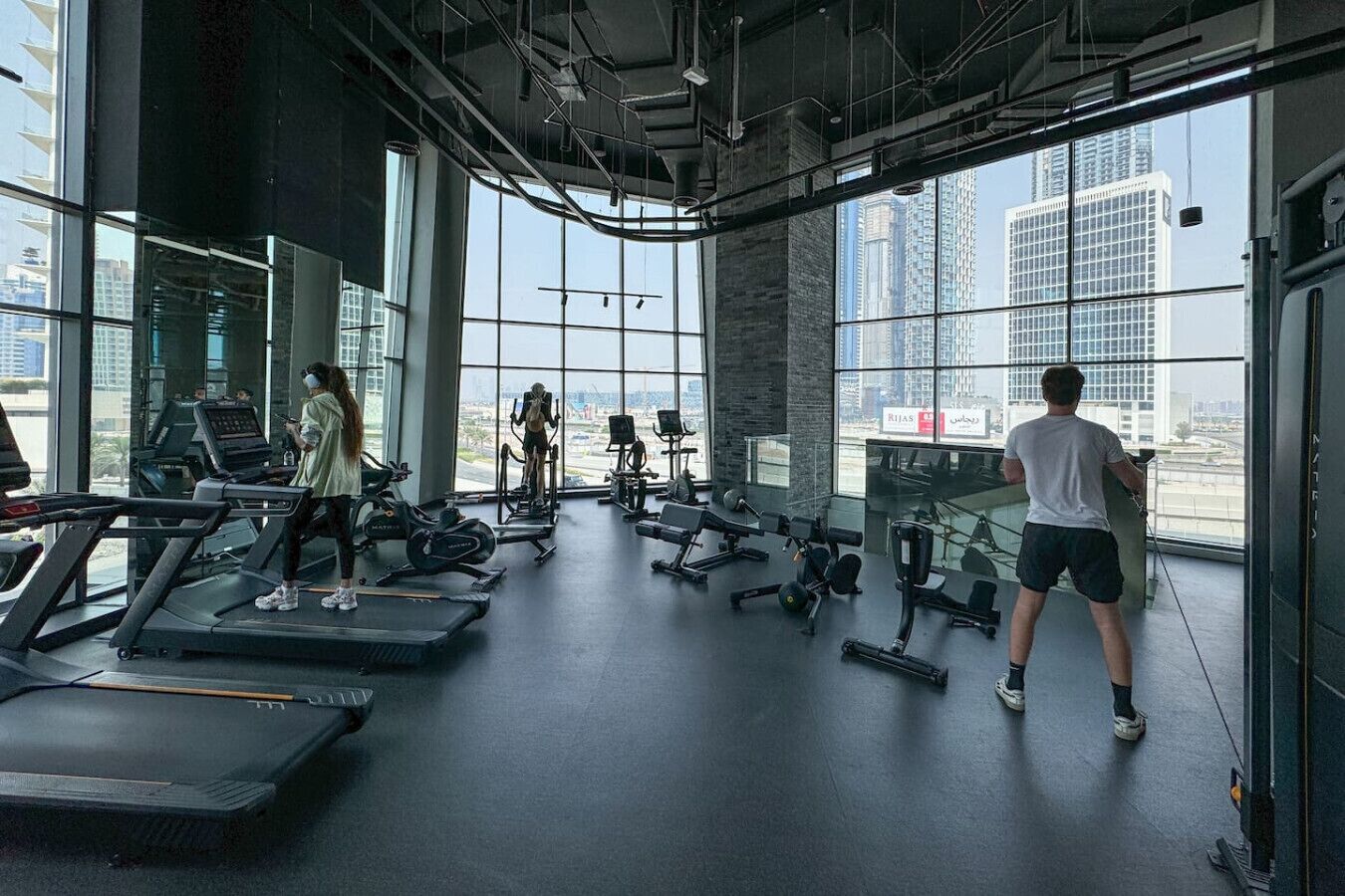 Une salle de sport équipée de tapis de course, d’appareils de musculation et dotée d’une grande fenêtre donnant sur un panorama urbain.