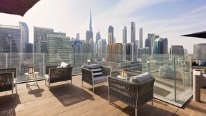 Eine Dachterrasse mit Korbmöbeln, einer Glasbrüstung und Blick auf die Stadtlandschaft.