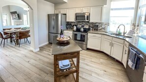 A modern kitchen with stainless steel appliances, a wooden dining table, and a view of the city through large windows.