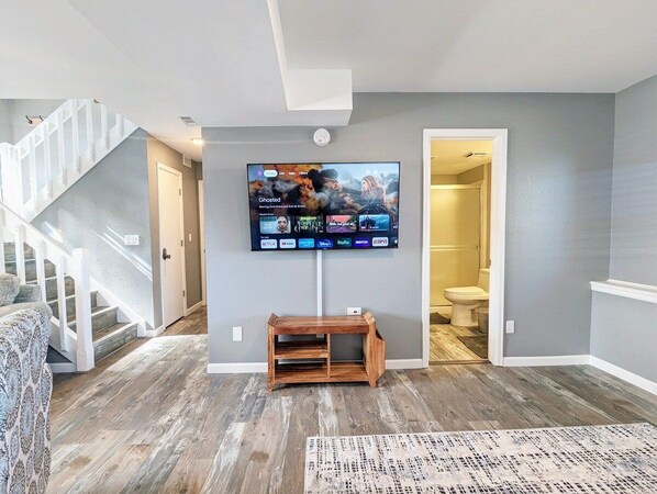 Una sala de estar con un televisor de pantalla plana montado en la pared, un banco de madera y una escalera que conduce a otra habitación.