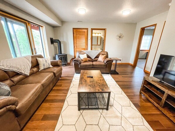 A spacious living room with a brown leather sofa, a wooden coffee table, and a TV on a wooden stand.