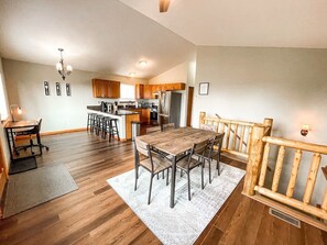 A spacious kitchen with wooden cabinets, a dining table with chairs, and a wooden railing.
