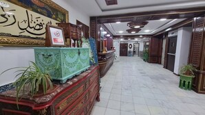 A hallway with ornate furniture, a large framed calligraphy piece, and potted plants. - Dar Diaf - El Djelfa (Djelfa)