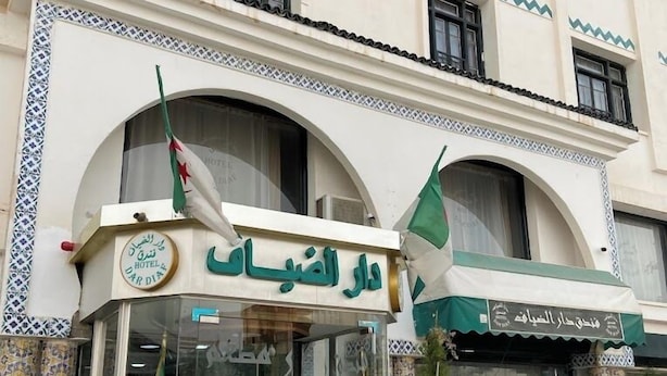 A hotel entrance with a sign in Arabic, flags, and potted plants. - Dar Diaf - El Djelfa (Djelfa)