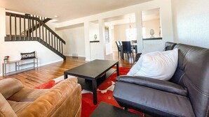 Un vaste espace de vie comprenant un escalier, un canapé en cuir noir, un divan en cuir marron et, au fond, un coin repas.