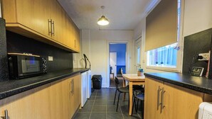 A compact kitchen with wooden cabinets, a microwave, a small refrigerator, and a window with blinds.