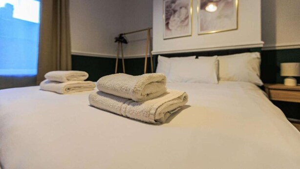 A neatly made bed with folded towels, a bedside lamp, and two framed pictures on the wall.