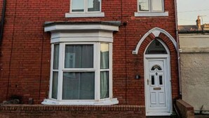 A red brick house with a bay window, a white door, and a chimney.