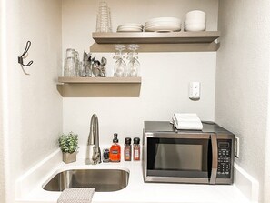 A compact kitchen with a sink, a microwave, and shelves above holding dishes and glassware. - Gateway Lodge Pool & Spa Studio | Walk to Lifts! (Keystone)