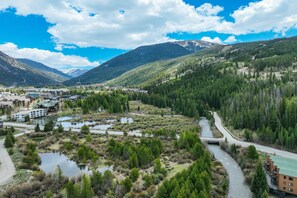 A mountainous landscape with a river, a bridge, and buildings with a green roof. - Gateway Lodge Pool & Spa Studio | Walk to Lifts! (Keystone)