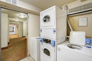 Un espace buanderie avec des lave-linge et des sèche-linge superposés, une porte visible donnant sur une autre pièce et un climatiseur fixé au mur.