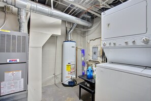 A utility room with a water heater, an air conditioning unit, and a table with cleaning supplies.