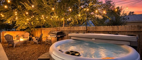 Un jardin avec un jacuzzi, du mobilier d’extérieur, des guirlandes lumineuses et une clôture en bois.