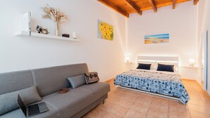 A bedroom with a bed, a grey sofa, a laptop, a small table with a vase and flowers, and a painting on the wall. - La Dolce Vita By Just Houses SRl (Torre Pali)