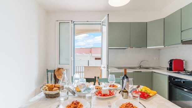 A modern kitchen with a dining table set for a meal, featuring various dishes and glasses. - La Dolce Vita By Just Houses SRl (Torre Pali)