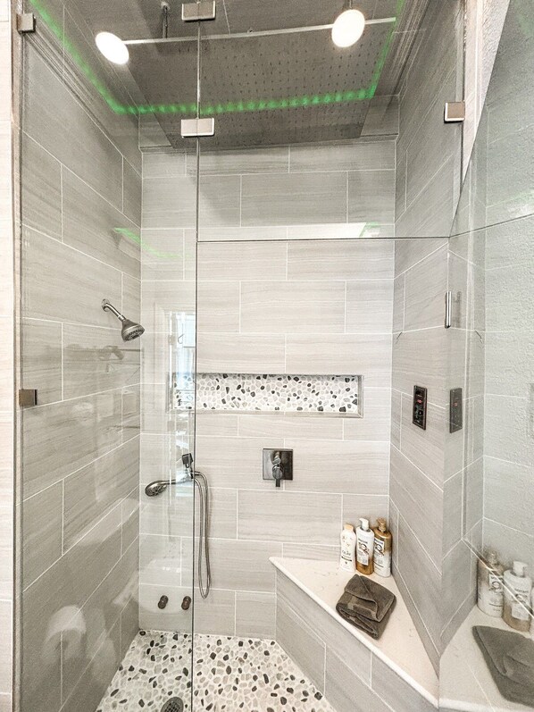 Una ducha moderna con puerta de vidrio, un panel de control y un estante pequeño con artículos de aseo.