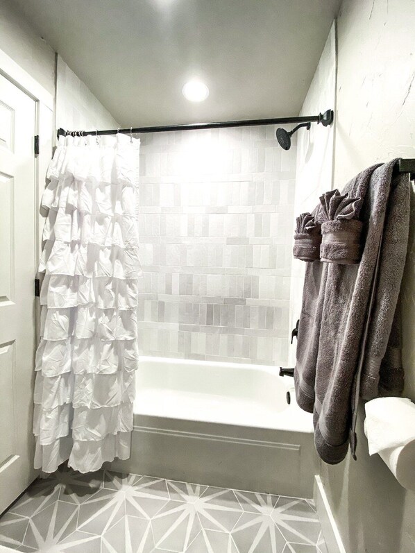 A bathroom with a white tiled shower, a geometric patterned floor, and two towels hanging on the wall.