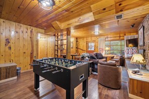 A cozy wooden interior with a foosball table, leather seating, and a fireplace.