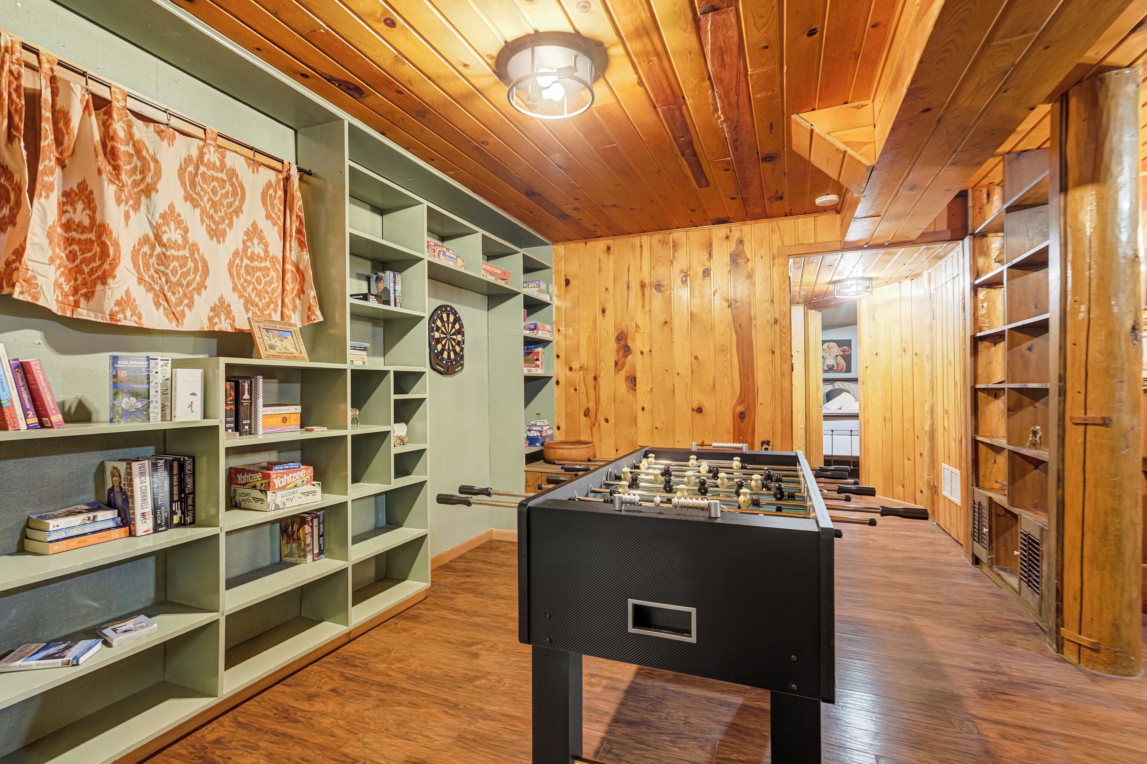 Ein Zimmer mit einer Fußball-Kicker-Tischplatte, Regalen mit Büchern und Spielen sowie einer Dartscheibe.