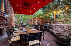 An outdoor patio with a stone wall, a wooden table set for dining, and a grill area.