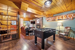 A cozy room with a foosball table, a fireplace, a television, and a wooden ceiling.