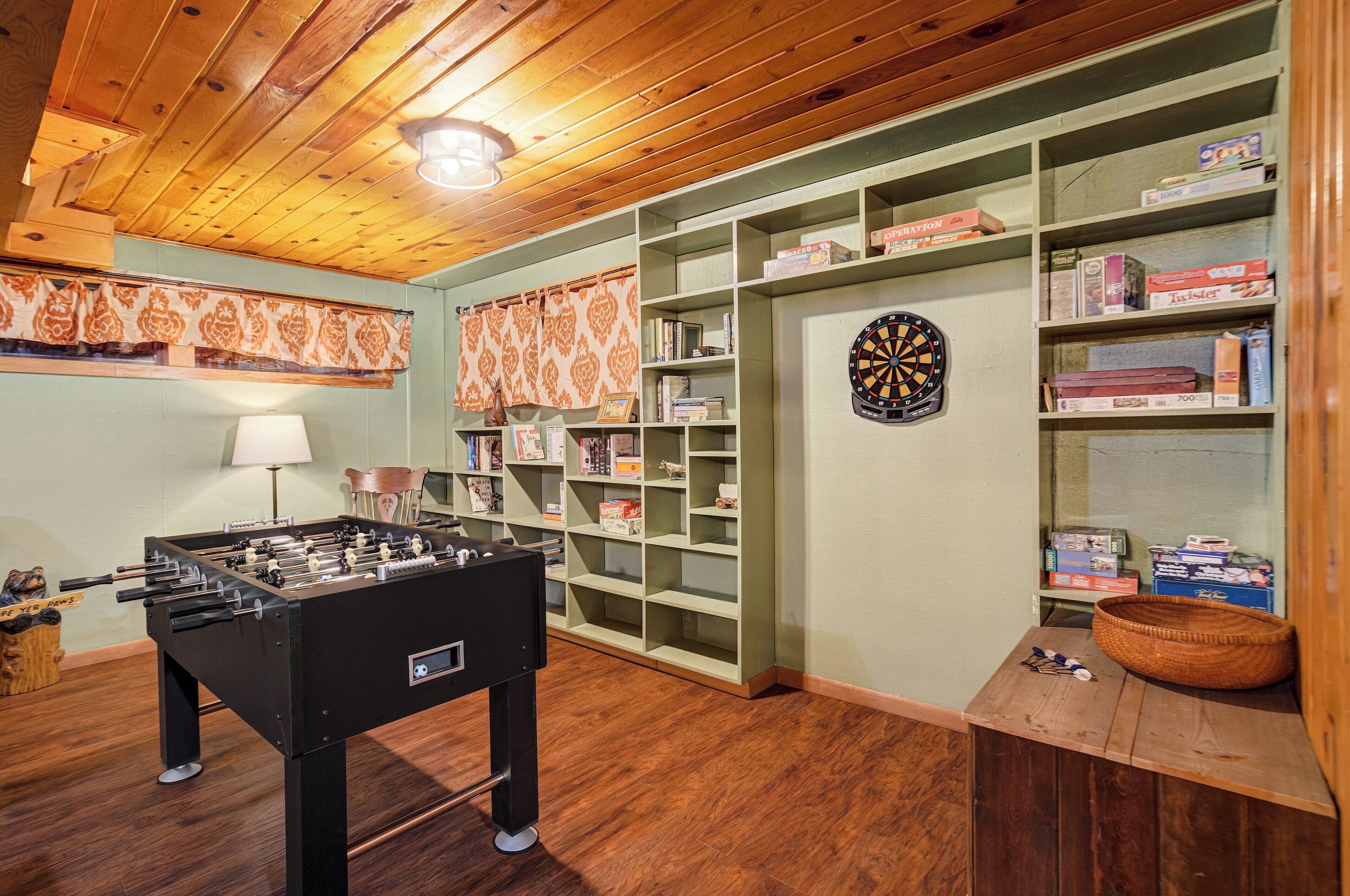 A room with a foosball table, shelves with board games, and a dartboard.