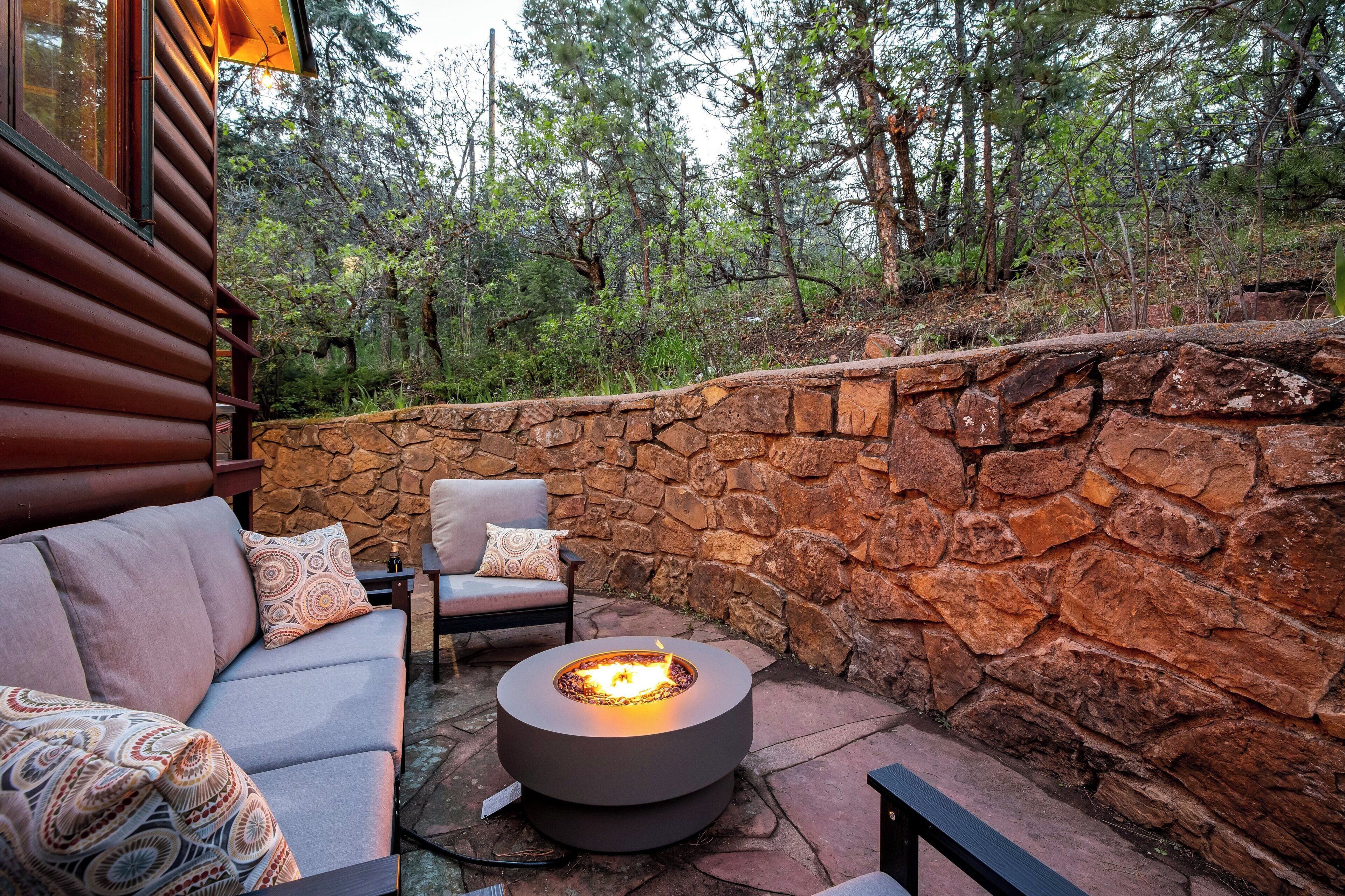 A stone wall, a round fire pit, and a sofa with cushions.