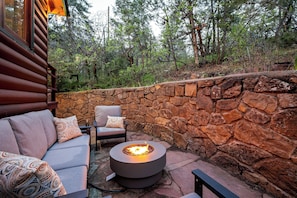 A stone wall, a round fire pit, and a sofa with cushions.
