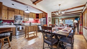 Una cocina con armarios de madera, un comedor con una mesa dispuesta para cuatro personas y una lámpara de araña grande.