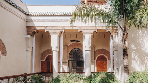 A courtyard with a tiled floor, white walls, and arches. There are two lounge chairs and a table. - Nobu Riad (Marrakech)