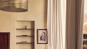 A living room with a sofa, a coffee table, a bookshelf, and a hanging light fixture. - Nobu Riad (Marrakech)