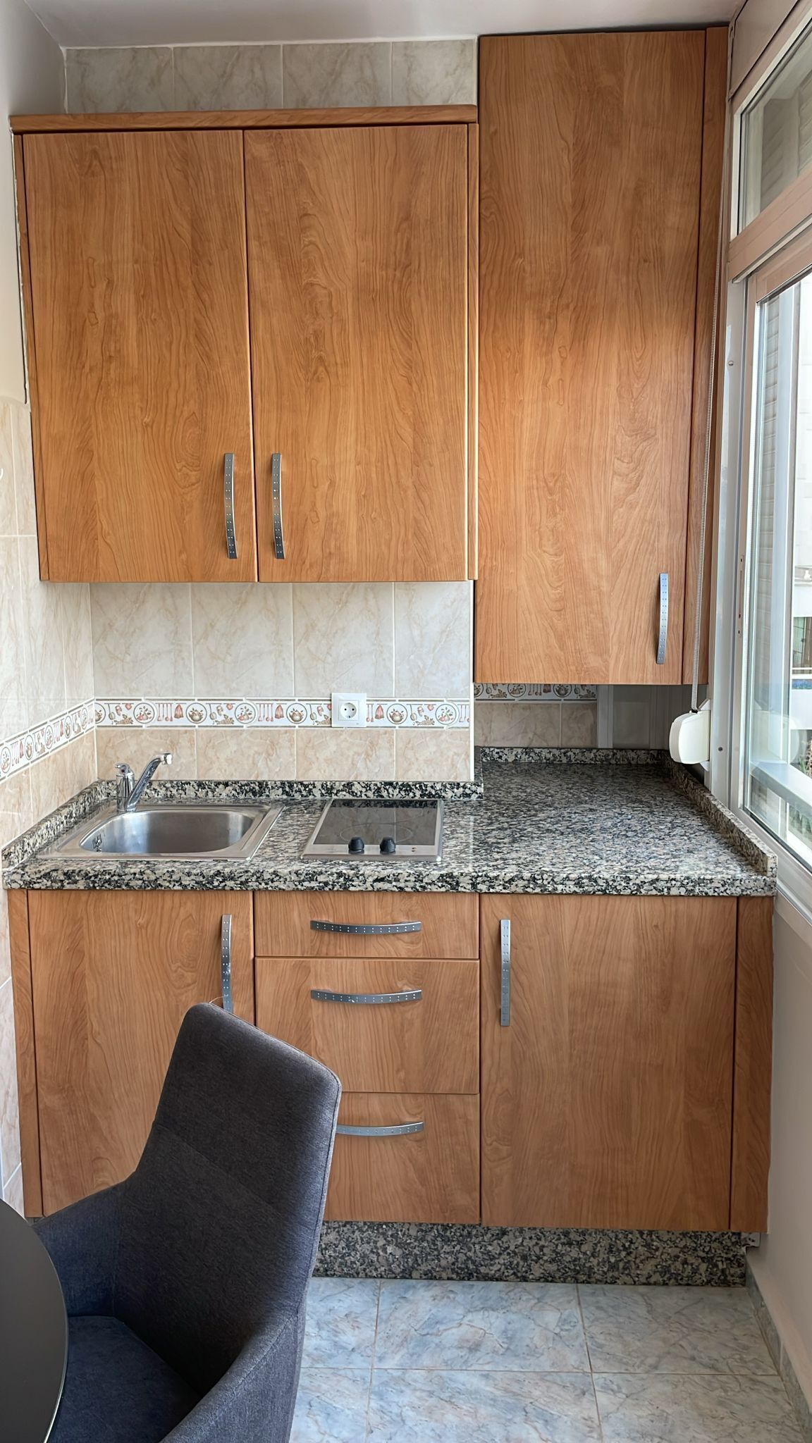 Een keuken met houten kastjes, een granieten aanrecht, een roestvrijstalen spoelbak en een raam met uitzicht.