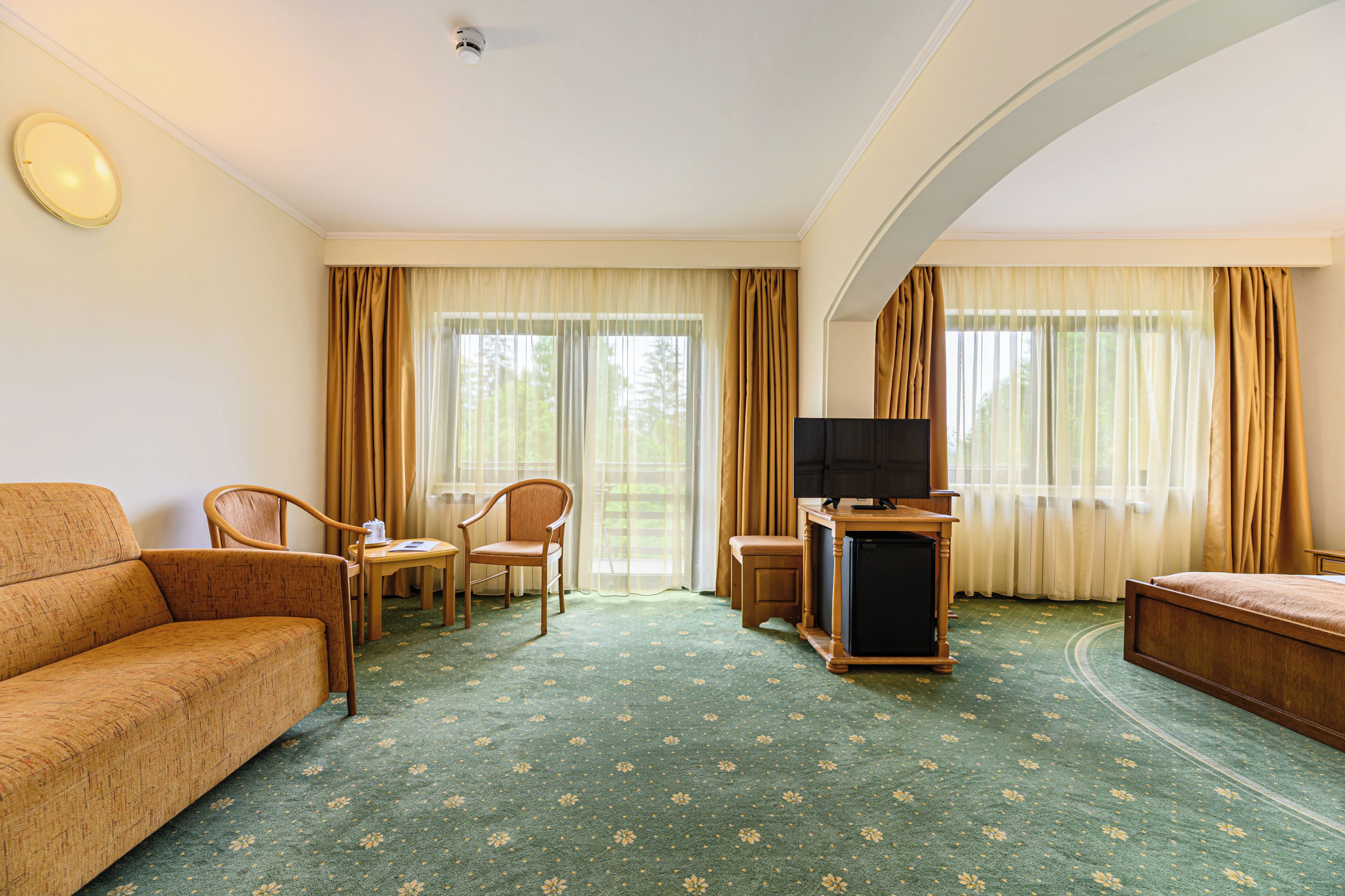 Una habitación de hotel con sofá, dos sillones, una mesita, televisor y cama.
