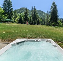 Un jacuzzi en una zona con césped y montañas al fondo.