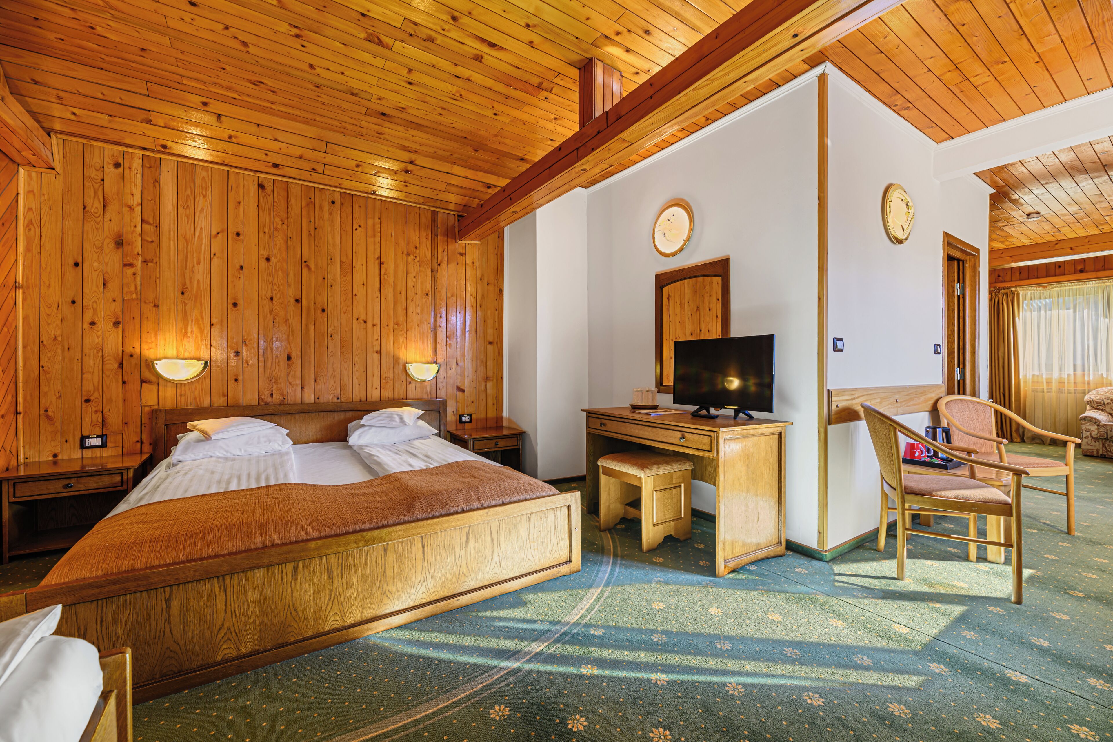 A wooden-paneled room with a bed, desk, chair, and television.