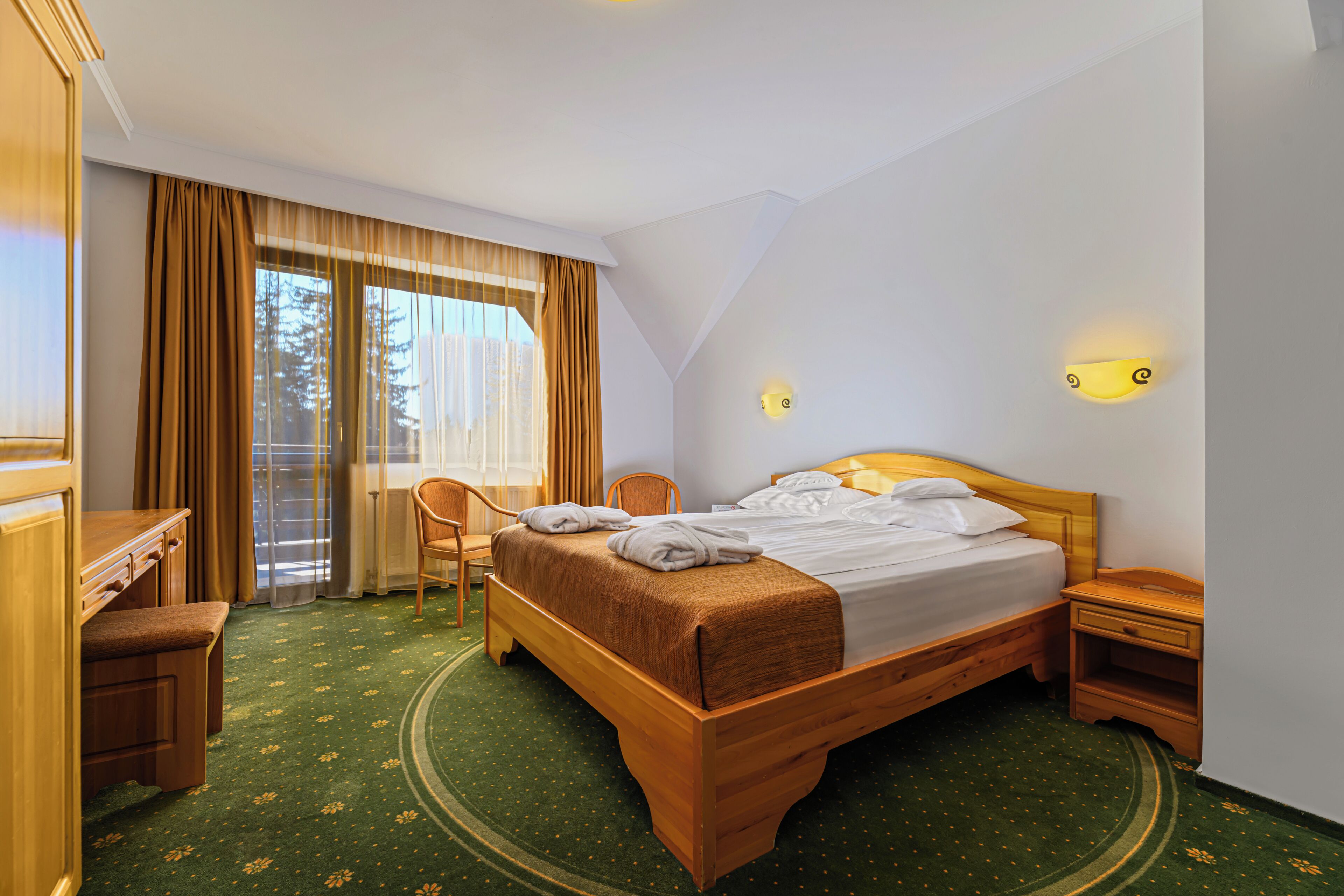 Habitación de hotel con una cama de madera, un escritorio, una silla y vistas al exterior a través de un ventanal grande.