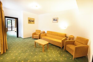 Una sala de estar con un sofá, dos sillones, una mesita de centro y una mesita auxiliar. Hay dos cuadros enmarcados en la pared.
