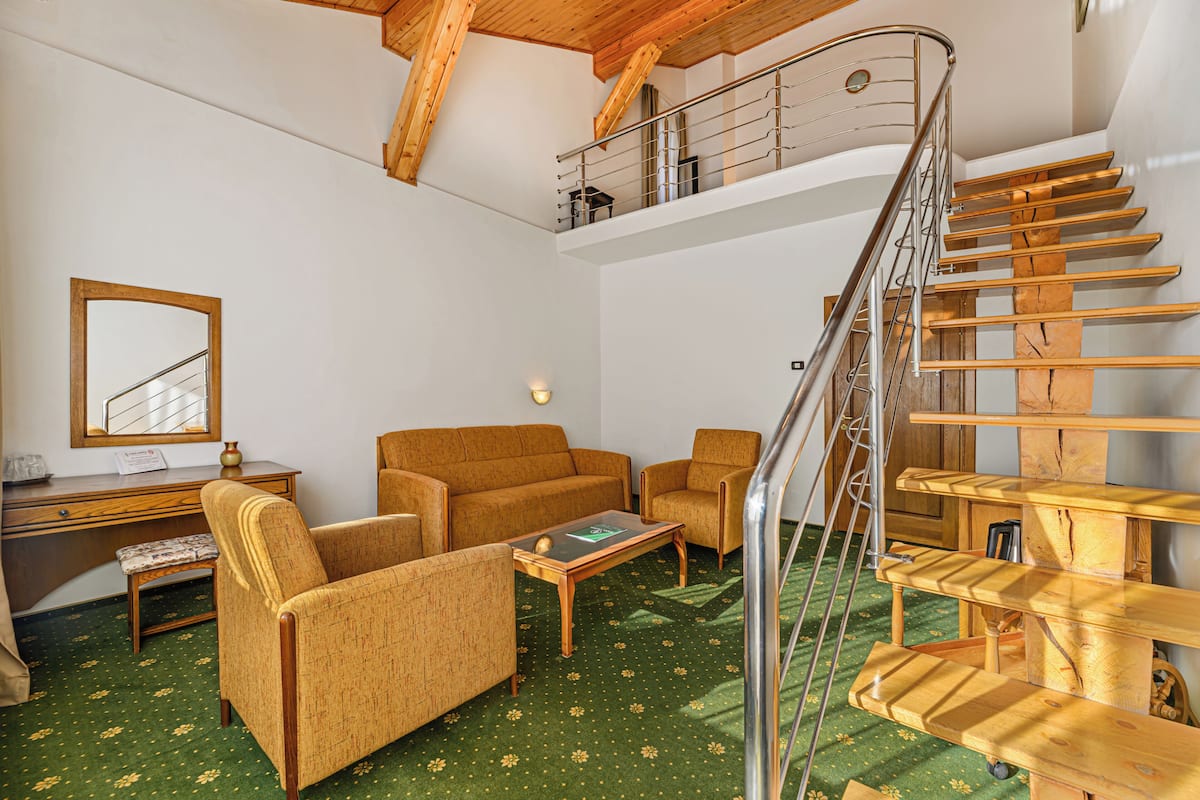 Ein geräumiger Wohnbereich mit einer Holztreppe, einer Sofagarnitur, einem Couchtisch und einem Schreibtisch mit Spiegel.