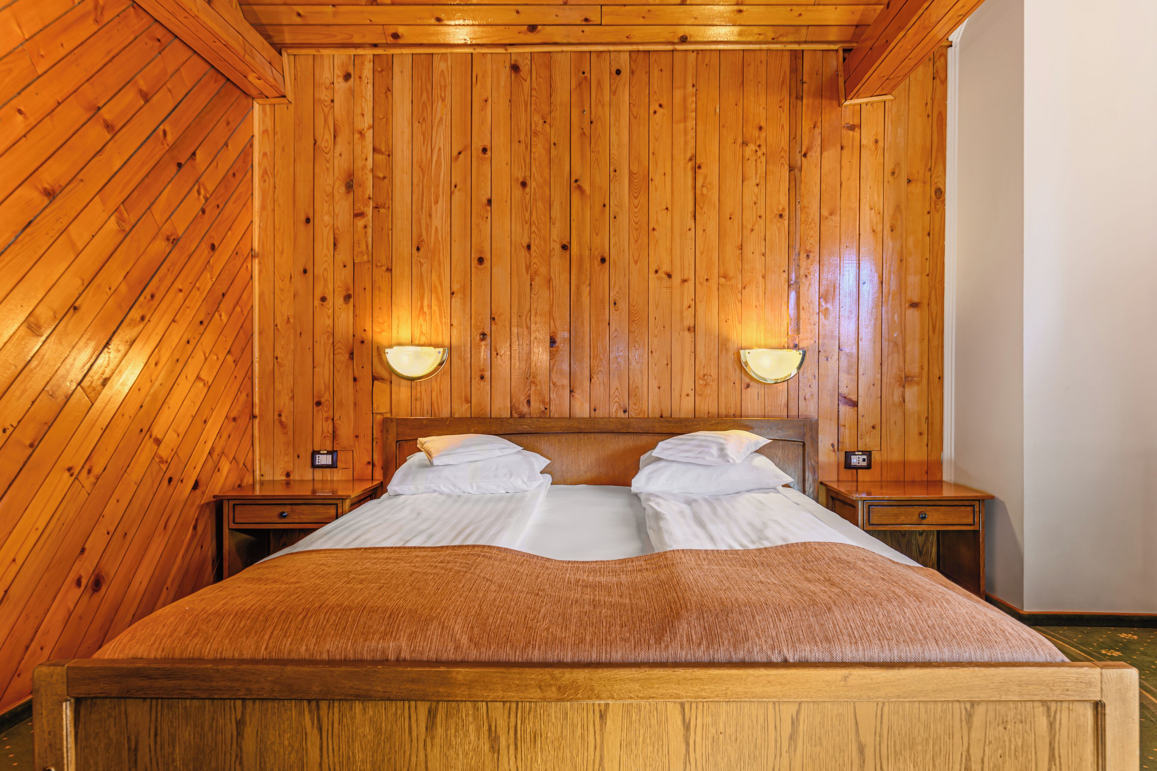 Een kamer met houten lambrisering, een bed, twee nachtkastjes en wandlampen.