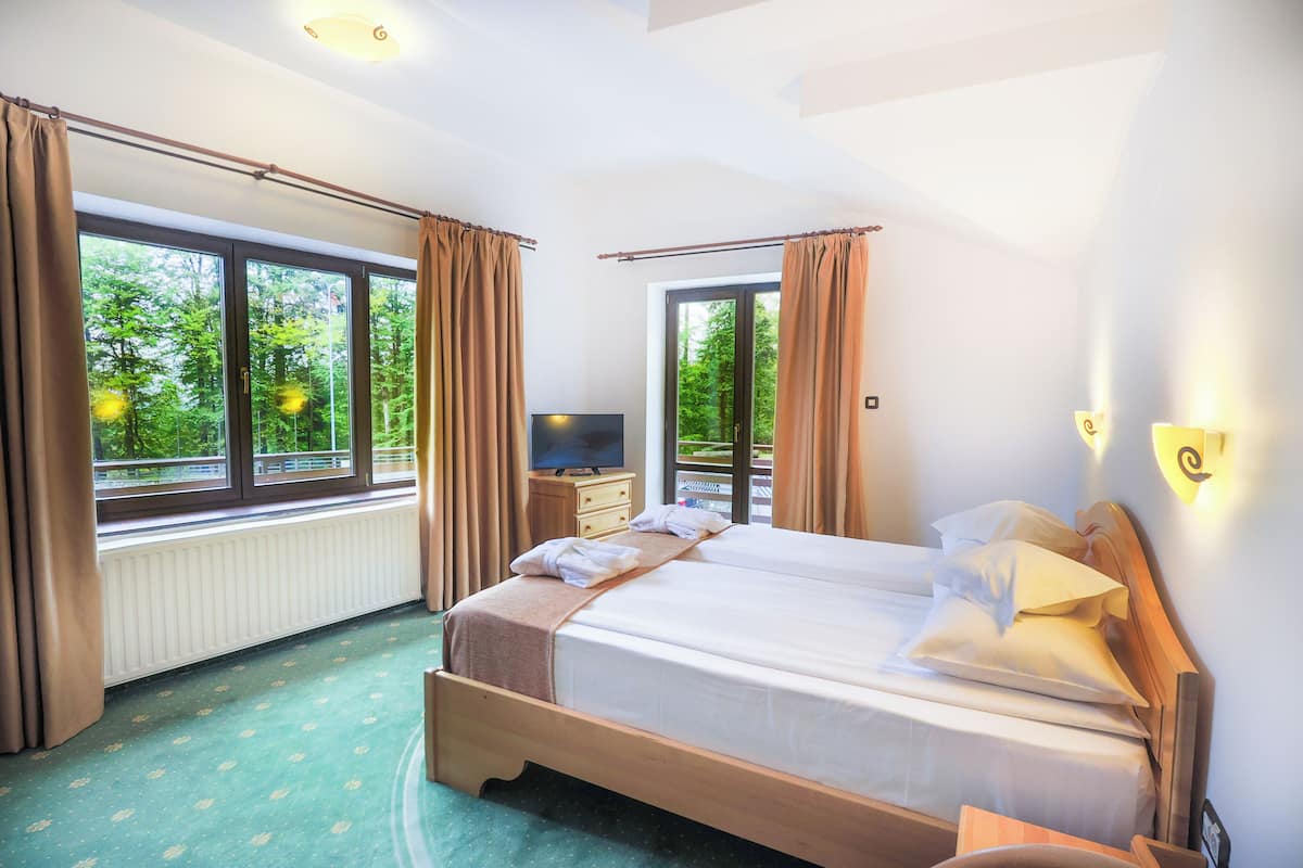 Ein Hotelzimmer mit einem großen Bett, einem Fernseher und Blick auf Bäume durch die Fenster.
