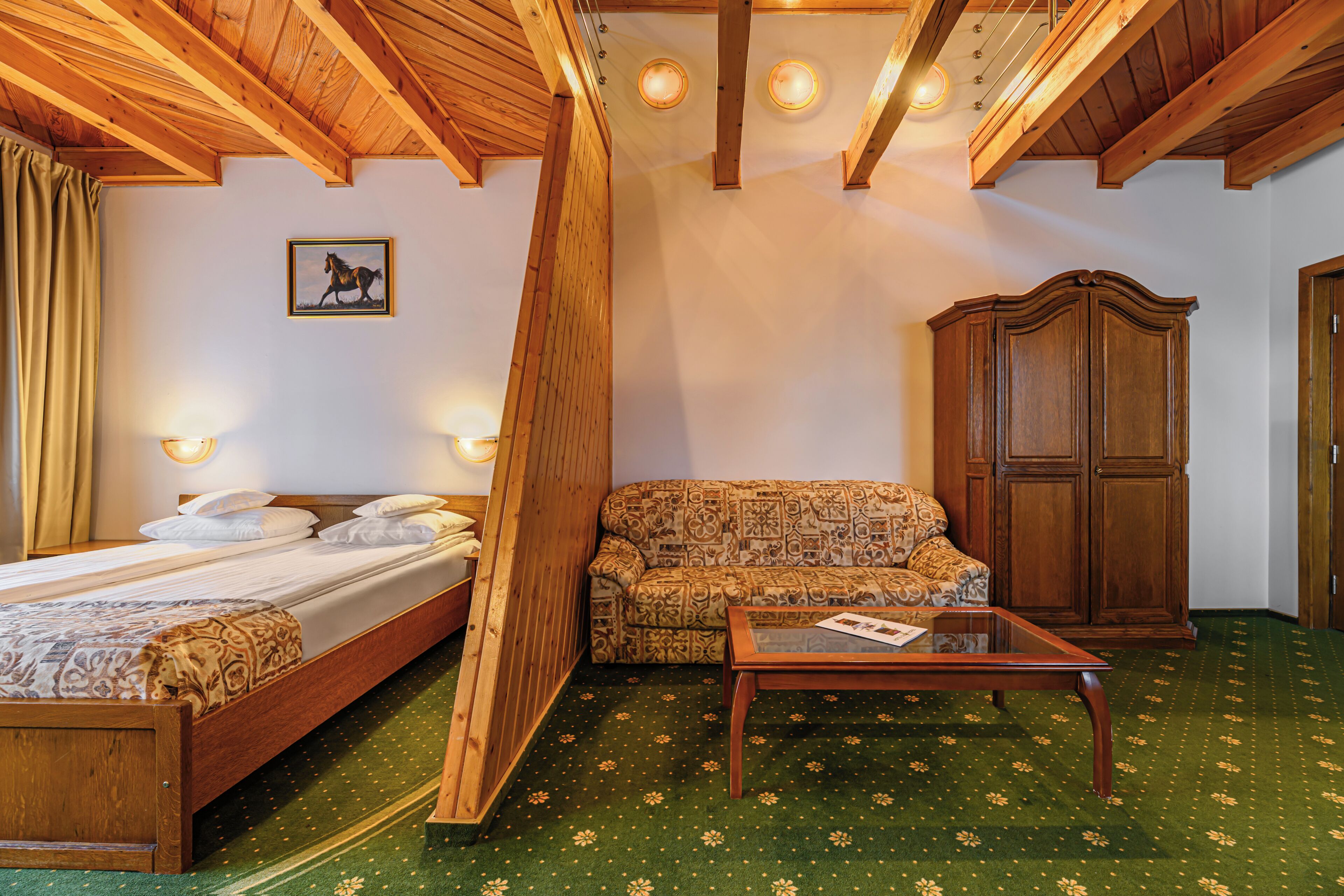 Una habitación con una cama de madera, un sofá estampado, un aparador de madera y una alfombra verde con motivos florales.
