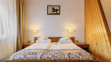 Una cama doble con una colcha estampada, dos mesitas de noche con lámparas, un cuadro enmarcado de un caballo en la pared y paneles de madera en el techo.