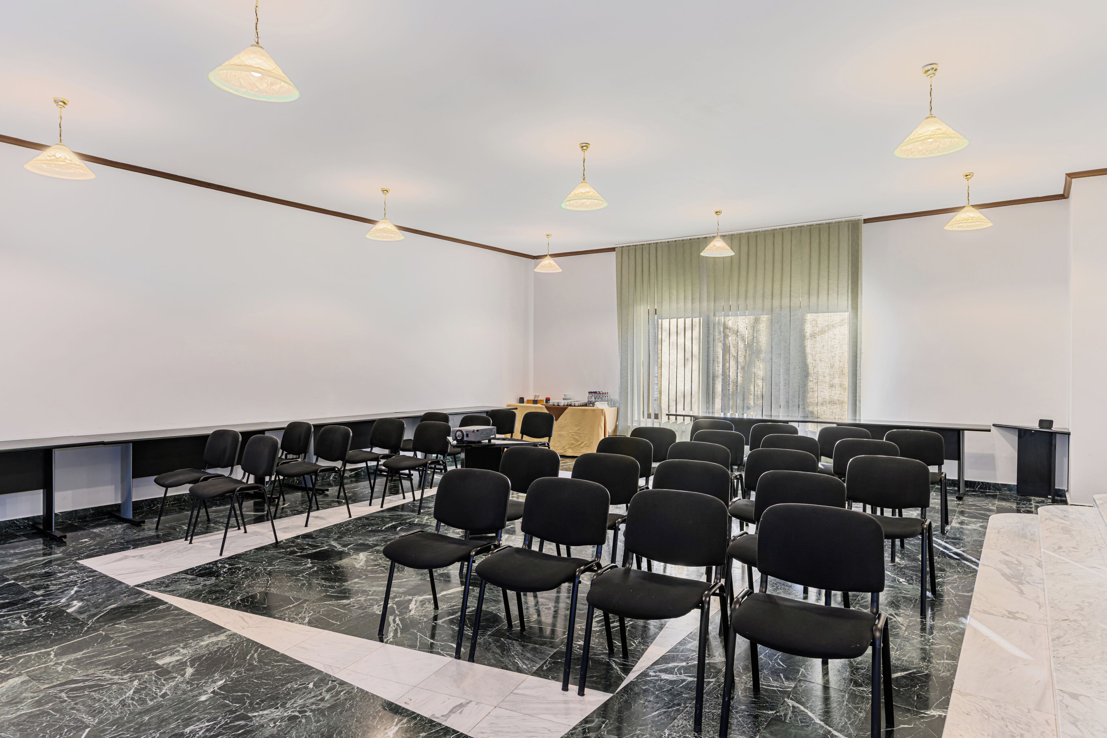 A conference room with a marble floor, black chairs arranged in rows, a projector, and a table with a screen.