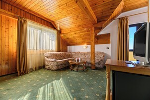 Una habitación acogedora con techo de madera, un sofá estampado, una mesita redonda y un televisor sobre un mueble de madera.