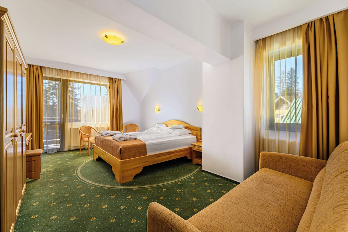 Ein Hotelzimmer mit Bett, Sessel, Schreibtisch und einem fenster mit Vorhängen.