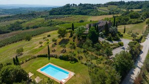 Une grande piscine rectangulaire, entourée d’une pelouse avec des arbres et un bâtiment en pierre en arrière-plan.