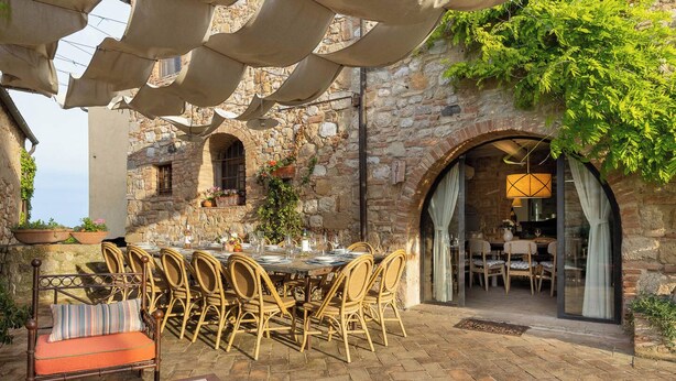 Un espace de restauration en plein air, avec un mur en pierre en arrière-plan, des chaises en osier et une table dressée pour un repas.