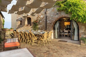 An outdoor dining area with a stone wall backdrop, wicker chairs, and a table set for a meal. - Exclusive Villa in San Gimignano with pool. (Toscana)